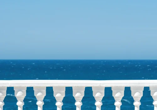 classic-roman-white-concrete-railing-outside-building-terrace-promenade-overlooking-sea-with-blue-sky-clouds copia