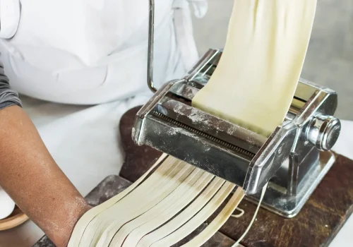 close-up-baker-cutting-raw-dough-into-tagliatelle-pasta-machine copia